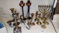 Full view of various metal candle holders including silver-plated candlesticks, brass menorahs and a pair of Mid-Century Modern style torches.