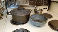 Cast iron Dutch oven, stone mortar, and metal mortar and pestle set arranged on stovetop.