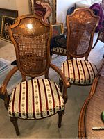 Front view of two wood frame dining chairs with carved top rail, cane backs, and upholstered seats with floral striped fabric.