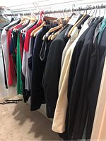 Multiple clothing items hanging on a rack showing variety of jackets, blouses, and sweaters
