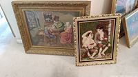 Two framed cross stitch artworks leaning against a wall, showing both pieces in context and relative size.