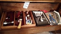 Drawer containing assorted silver-tone flatware pieces including forks, spoons, cutting utensils with Bakelite handles, and other kitchen utensils.