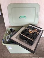 Light green plastic storage bin with lid open showing contents including countertop paint kit, IKEA style frames, and door stops