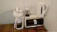 Protector Silex coffee maker, French press, electric kettle, and Black and Decker toaster oven together on table.
