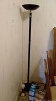 Full view of 71-inch torchier floor lamp with black finish and upward-facing bowl shade, positioned near wall and dining chairs