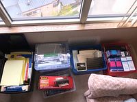 Photo of bins with folders, file holders, laminator box, and various office supplies on a windowsill