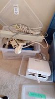Clear plastic bins containing multiple white power bars, power cords, and cables. One bin is open revealing the Linksys RE6700 device and cables.