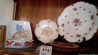 Display of assorted ceramics on wooden shelf including plates, a bowl, and a wooden tray