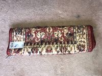 Folded woven rug showing the texture and pattern in red, cream, and brown shades.