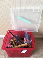Red plastic storage bin filled with assorted hand tools and accessories including a hammer and measuring tapes.