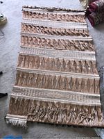 Full view of wool wall hanging laid flat on floor showing striped pattern and fringed edges.