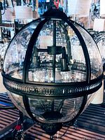 Full view of the spherical chandelier showing transparent glass globe panels and black metal framing with decorative horizontal band. Three internal light sockets visible.