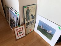 Group photo showing multiple framed art prints and posters leaning against wall including Adirondack chairs photo and Emily Carr exhibition poster.