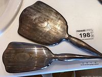 Top and back view of the hand mirror and brush side by side showing shape and tarnish