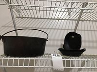 Cast iron 5 quart Dutch oven without lid and stack of four square cast iron serving dishes on a white wire shelf.