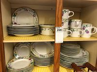 Shelf with stacks of various plates, bowls, cups, and saucers showing the floral vine pattern and gold rim detailing.
