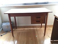 Full frontal view of teak desk with two drawers and tapered legs