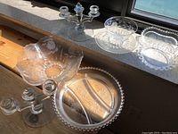 Overview of various clear glass serving dishes including bowls, divided plates, and dishes with etched floral and beaded designs, placed on window ledge.