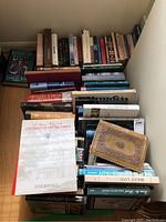 Stack of assorted hardcover and paperback books on the floor against wall