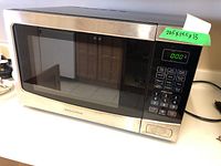 Front view of Insignia microwave oven showing stainless steel front and control panel with LED display.