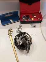 Photo showing Simpsons red jewellery box with pins and small salt spoon pin, brass horse head letter opener, and decorative bird cage globe.