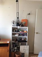 Wide shot showing the white wooden shelf with its contents and surrounding items including wastepaper baskets and a wooden cabinet.