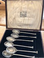 Six spoons in open presentation box showing satin liner and velvet bed