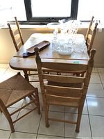 Wooden dropleaf table with four wooden chairs with woven seats around it, showing the overall set and condition.
