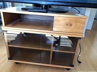 Front view of teak TV cabinet showing open shelf, small drawer with pull knob, and glass sliding doors with shelves inside.
