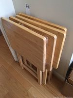 Four wooden TV tables stacked upright showing full shape and folding legs