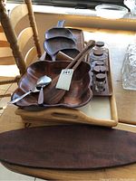 Wooden salad servers with square bowl, palm-shaped dish, teak trays with glass jars and spice shakers on a table