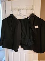 Two black men's suit jackets size 38R hanging on hangers on a door with three pairs of black dress pants.