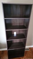 Front view of tall dark wood bookcase with four adjustable shelves and visible peg holes for adjustments.