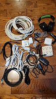 Lot contents including cables, extension cord, charger, headset on wood floor