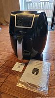 Frigidaire black digital air fryer with front handle and control panel, manual placed beside it on the floor.
