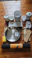 Kitchen lot items arranged on floor including porcelain bowls, frying pan, chopsticks, plates, and rolling mats.