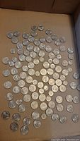 Loose US state quarters and other US coins spread on cardboard surface.