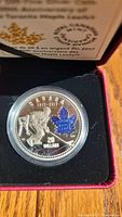 Close-up photo of the 2017 Royal Canadian Mint $20 silver coin commemorating the Toronto Maple Leafs 100th Anniversary, held in protective capsule and plated with detailed designs including a hockey player and blue maple leaf.