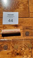 Photo of the full roll and the four loose pennies on a wooden surface with a MaxSold auction sticker.