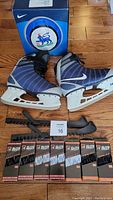 Pair of Nike ice skates size 8US in blue and gray, skateguards, and seven packs of ice skate laces on wooden floor