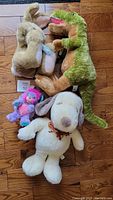 Four plush toys including Snoopy dog, dinosaur, bunny, and Popple arranged on wood floor.