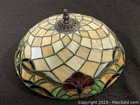 Side angle view of the dome-shaped stained glass lamp shade highlighting beige glass tiles, green vine pattern, and red floral accents with decorative metal top finial.