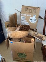 Photo showing boxed and unboxed woven baskets, carved wall art, and hand broom grouped together in a cardboard box.