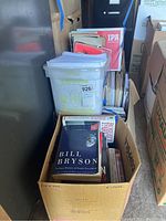 Shows cardboard box with books including Bill Bryson title and plastic container with magazines and papers