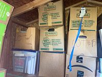 Stack of U-Haul cardboard boxes mostly filled with books and other items, some handwritten markings on boxes.