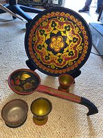 Painted wooden ladle, two cups including one larger, all decorated with floral and geometric designs in red, yellow, black and gold colors.