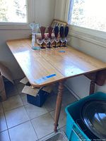 Wooden dining table with one drop-leaf partially extended, showing rectangular tabletop and turned wooden legs