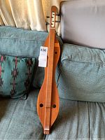 Full view of the wooden dulcimer resting on couch, showing teardrop body and tuning pegs.