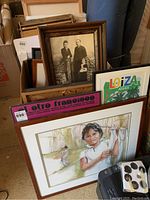 Stack of framed wall art including colorful prints and a woodcut-style print in wooden frame