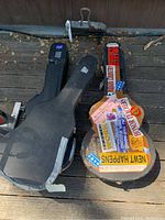 Three guitar cases on wooden floor, one guitar covered with colorful stickers visible with case open.